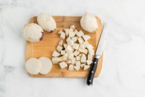 A cutting board with three whole peeled turnips and a pile of diced turnips next to a knife.