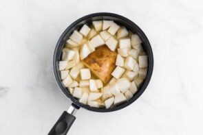 A saucepan with a half a potato surrounded by diced turnips in water.