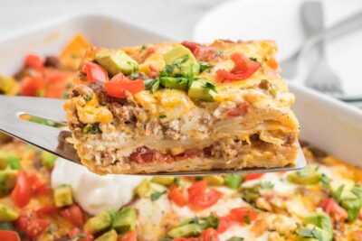 A spatula holding a slice of mexican breakfast casserole with layers of tortilla, sausage and cheese.