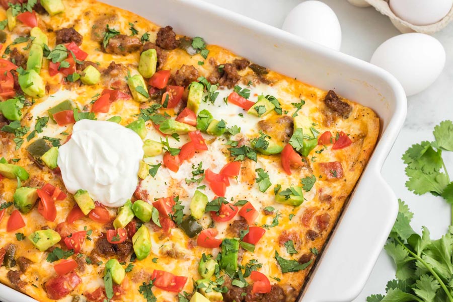 Looking down on an egg casserole filled with sausage, bell pepper and topped with sour cream and avocado.