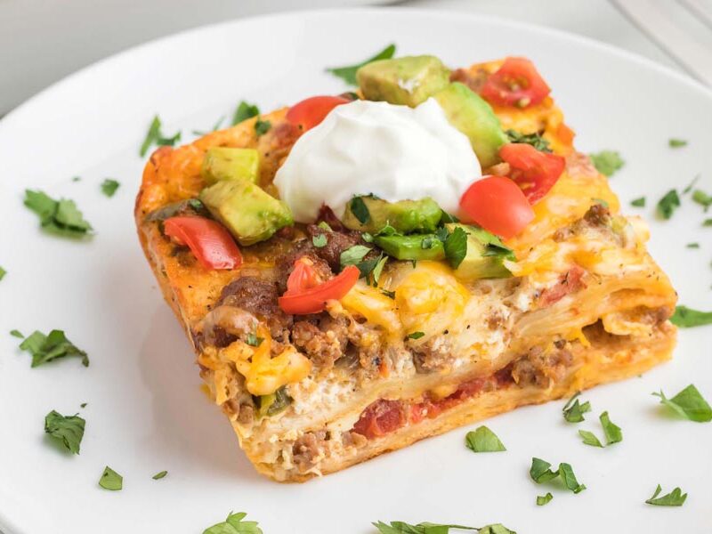 A slice of breakfast casserole on a plate with cilantro scattered around.
