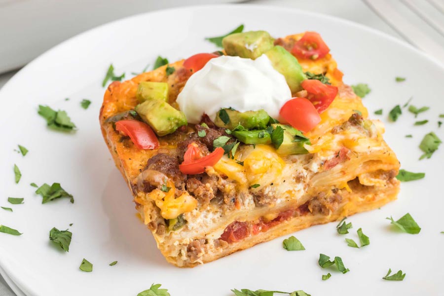 A slice of breakfast casserole on a plate with cilantro scattered around.