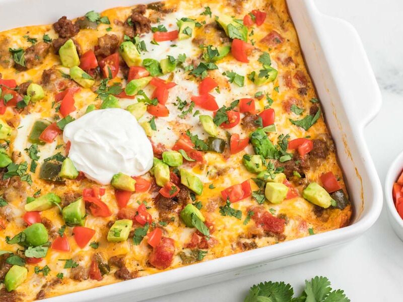 Colorful casserole topped with avocado, sour cream, tomato and cilantro.