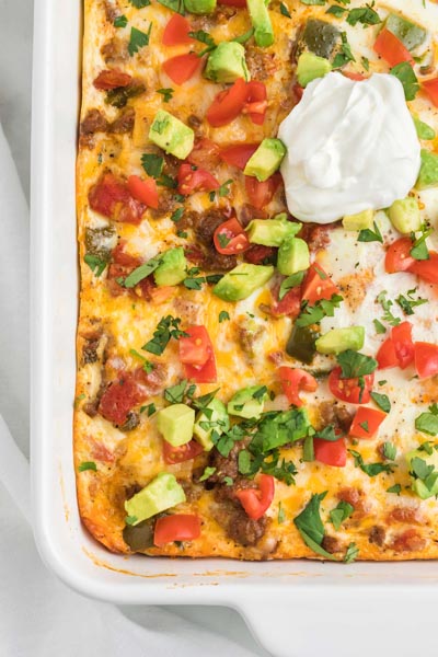 Looking down into a casserole dish filled with an egg based casserole topped with avocado, tomato and sour cream.