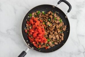 A skillet with cooked sausage, bell pepper and diced tomatoes poured on top.