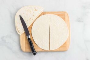 Flour tortillas cut in half on a cutting board with a knife next to it.