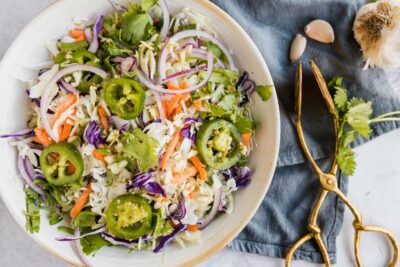 a bowl of coleslaw topped with jalapenos, red onions and cilantro