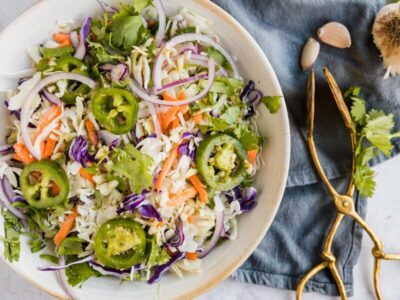 a bowl of coleslaw topped with jalapenos, red onions and cilantro
