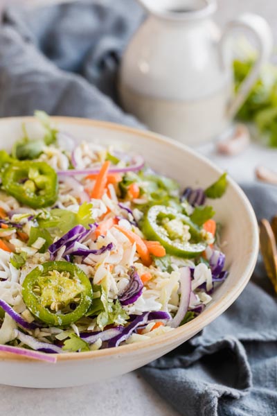 A bowl of spicy mexican coleslaw in front of a dressing boat.