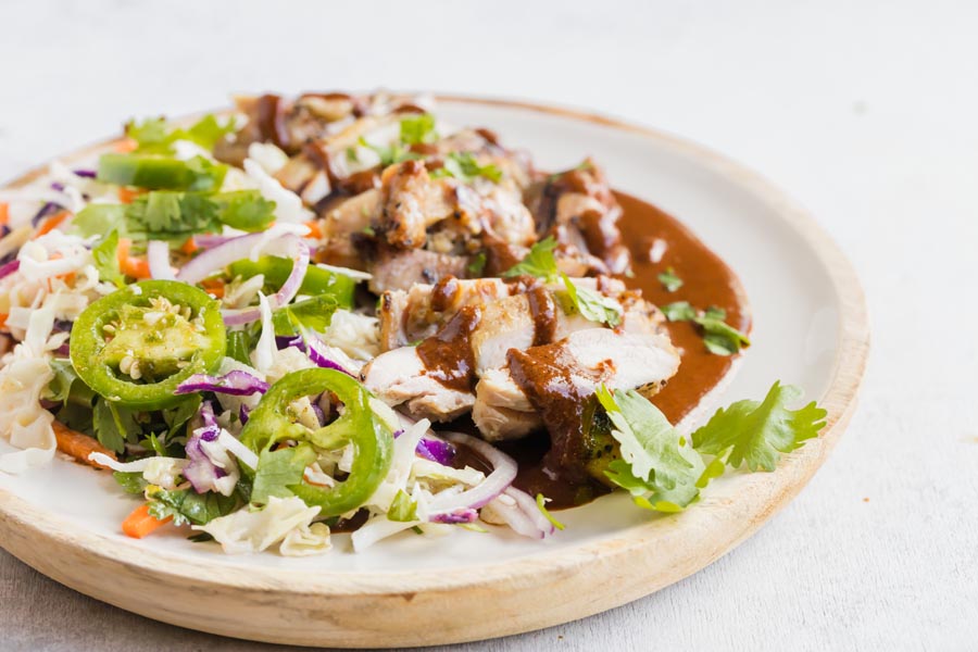 A plate with coleslaw and jalapenos next to chicken covered in mole sauce.