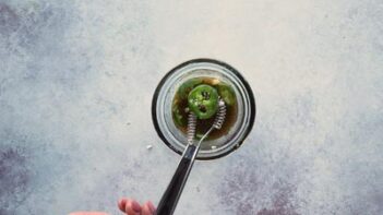 A flat whisk pulling out a jalapeno slice over a small bowl of dressing.