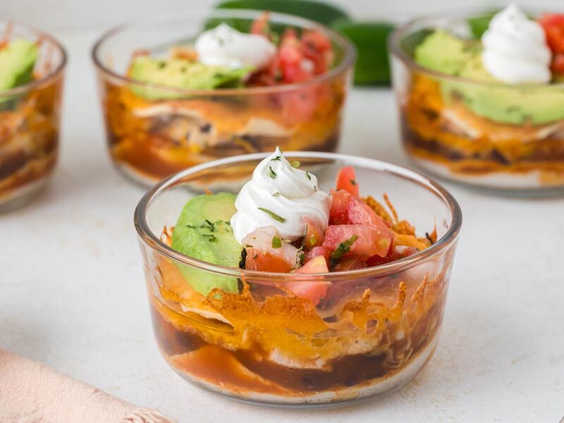 Individual Mexican lasagna bowls topped with avocado, salsa and sour cream.