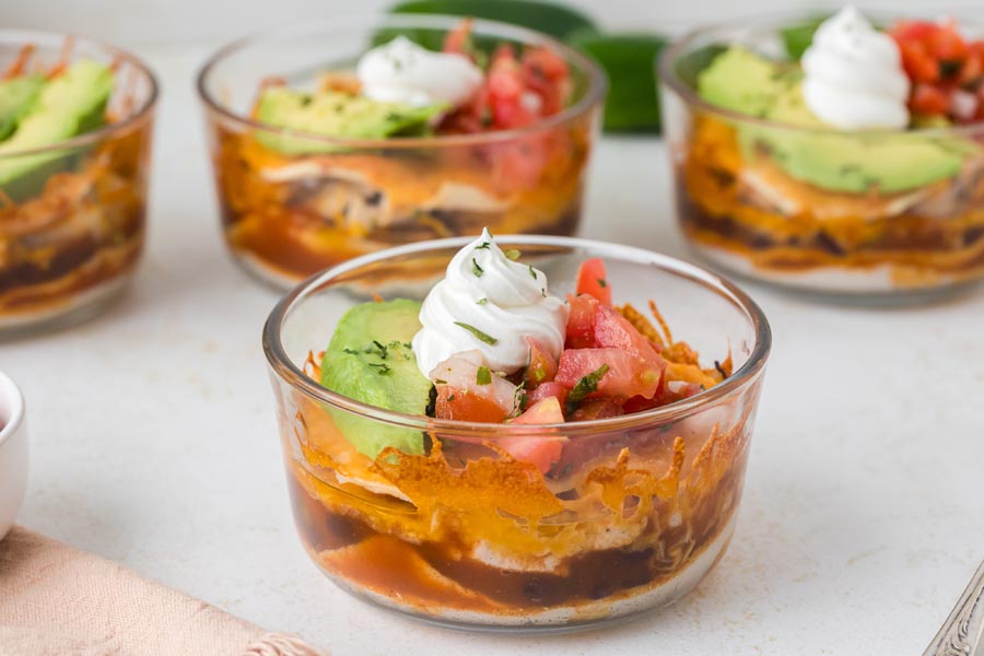 A single Mexican lasagna bowl garnished with sour cream and avocado, with more bowls in the background.