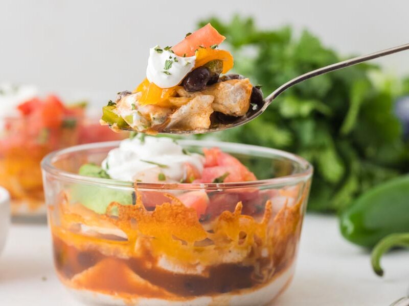 A spoonful of layered chicken, beans, and toppings being lifted from a lasagna bowl.