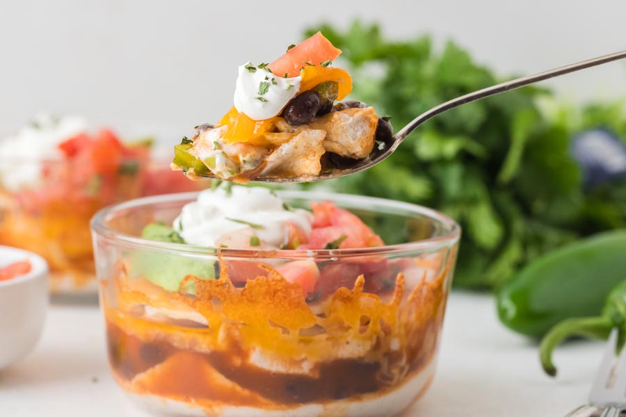 A spoonful of layered chicken, beans, and toppings being lifted from a lasagna bowl.