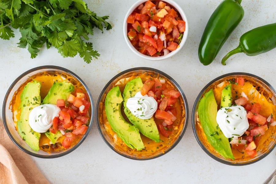 Overhead view of three Mexican lasagna bowls garnished with avocado slices and sour cream.