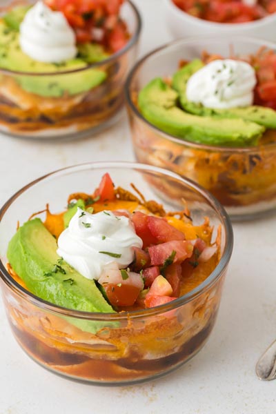 Multiple glass bowls filled with layered Mexican lasagna ingredients, each topped with fresh toppings.