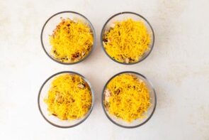 Step showing shredded cheddar cheese layered on top of the lasagna mixture in each bowl.