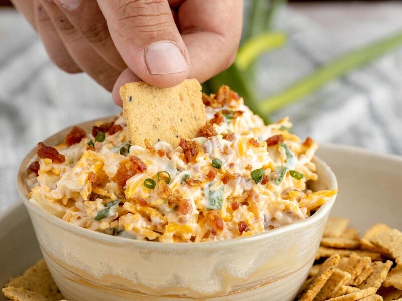 dipping a crackers into a bacon and cheese dip
