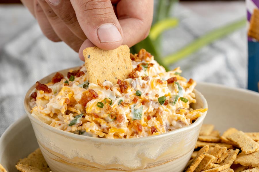 dipping a crackers into a bacon and cheese dip