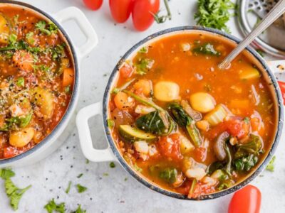 a spoon in a small bowl of tomato based minestrone soup