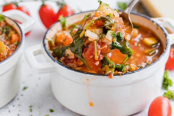 a spoonful holding a soup with a bunch of vegetables