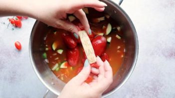 holding a rind of parmesan cheese over a pot with peeled tomatoes