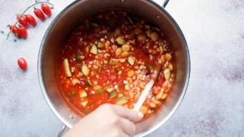 stirring a pot of minestrone soup filled with vegetables