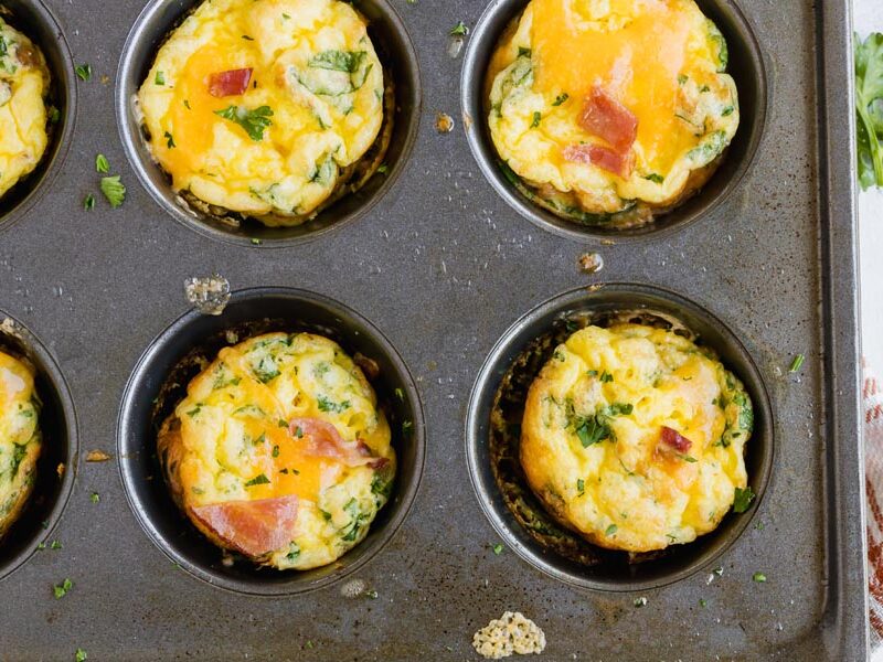 mini egg muffins in a muffin tin topped with cheese, bacon and parsley