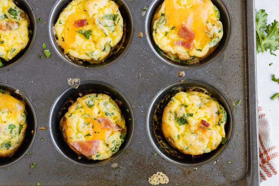 mini egg muffins in a muffin tin topped with cheese, bacon and parsley