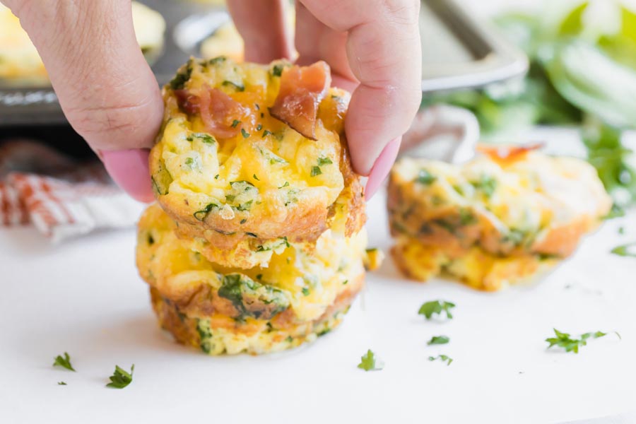 holding a mini frittata in between fingers with two other bite sized frittatas in the background