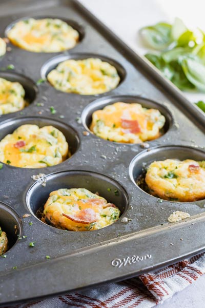 egg frittatas in a muffin pan with spinach in the background
