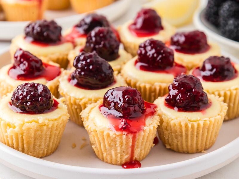 A group of mini cheesecakes topped a blackberries and syrup.