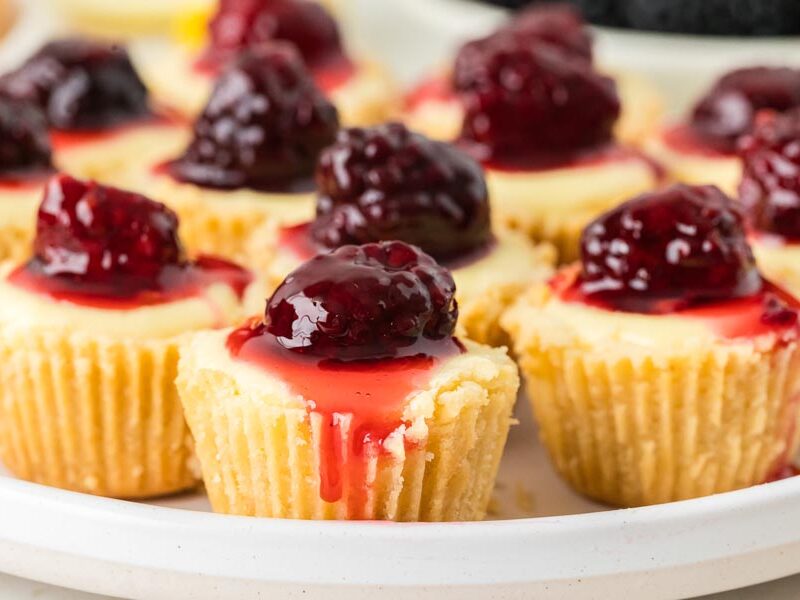 Syrup dripping down a mini cheesecake bite topped with a blackberry.