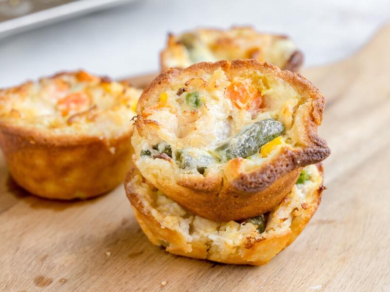 Two mini keto chicken pot pies stacked to show the creamy chicken, carrots, peas, and green beans inside the crisp crust.