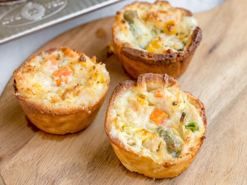 Three homemade mini keto chicken pot pies with golden crusts and creamy chicken and vegetable filling on a wooden board.