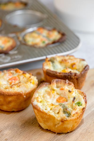 Freshly baked mini keto chicken pot pies on a wooden board with a muffin tin in the background.