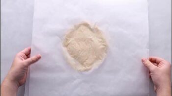 Keto pot pie dough placed between two sheets of parchment paper before rolling.