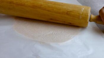 Keto pot pie dough being rolled thin between sheets of parchment paper with a rolling pin.