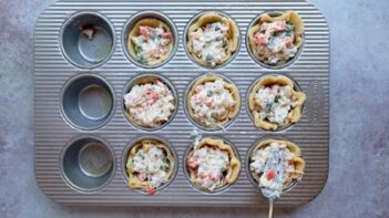 Keto pie crusts in a muffin tin being filled with the creamy chicken and vegetable pot pie mixture before baking.