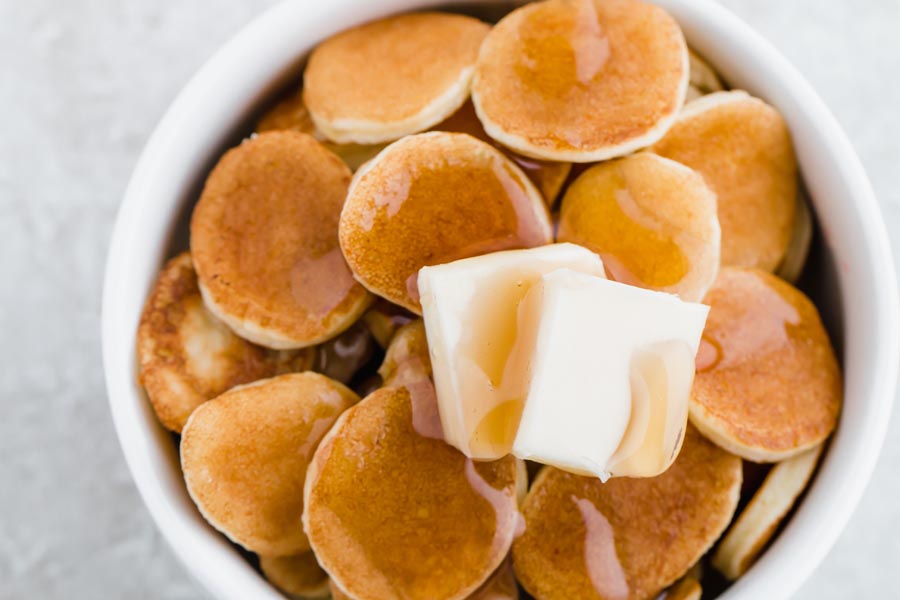 multiple little gluten-free pancakes in a bowl with butter and syrup on top