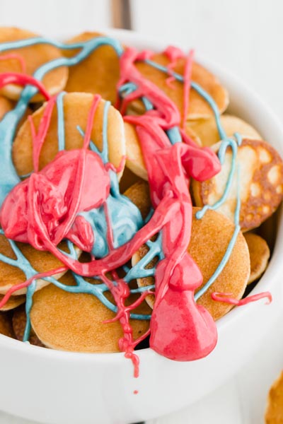 melted chocolate colored red and blue drizzled over a bowl of mini pancakes