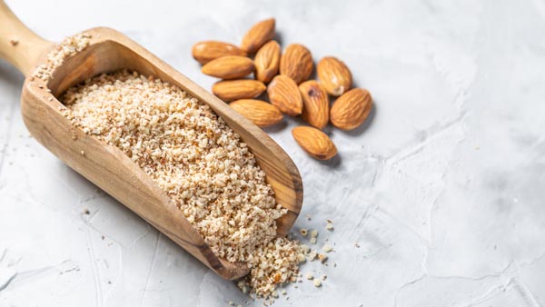 a scoop of almond flour next to some whole almonds on the counter
