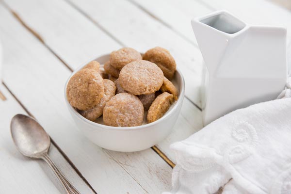a bowl of cookie cereal with a small carton of milk and a spoon