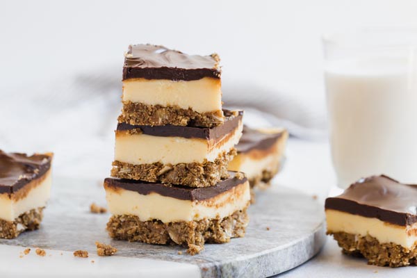 nanaimo bars stacked on each other on a marble slab with more bars next and crumbs