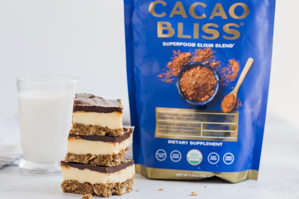a bag of cacao bliss next to three nanaimo bars and a glass of milk
