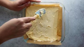 spreading a butter cream custard layer in a square baking dish with a spatula