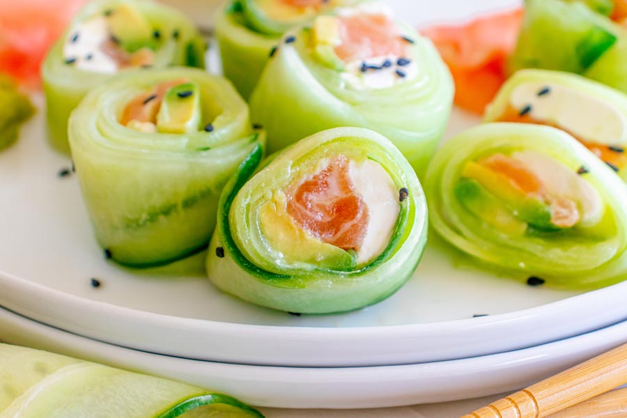 Cucumber rolls filled with sockeye salmon and cream cheese on a stack of white plates.