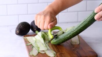 Peeling an English cucumber with a vegetable peeler into long thin strips.