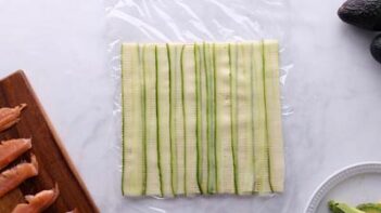 Thin strips of cucumber slices overlapping and lined on top plastic wrap.